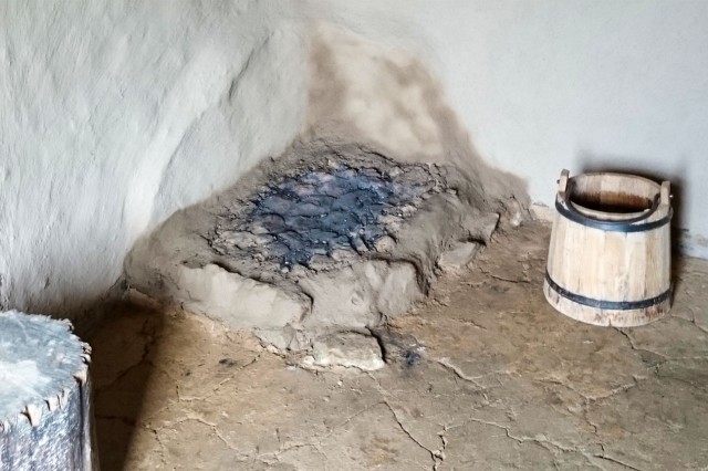 Rekonstruktion einer mittelalterlichen Feuerstelle in der Hausecke. Gut erkennbar ist die zusätzliche Lage Lehm zum Schutz der Außenwände. (Geschichtspark Bärnau-Tachov)